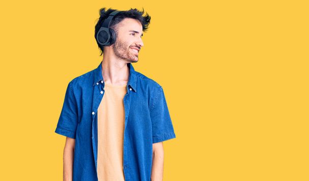 若いヒスパニック系の男性の音楽をヘッドフォンを離れて顔に笑みを浮かべて横に見て、自然な表現を聞いて。自信を持って.  - 写真・画像