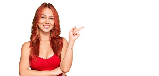 Young redhead woman wearing casual clothes with a big smile on face, pointing with hand and finger to the side looking at the camera.  - Foto, immagini