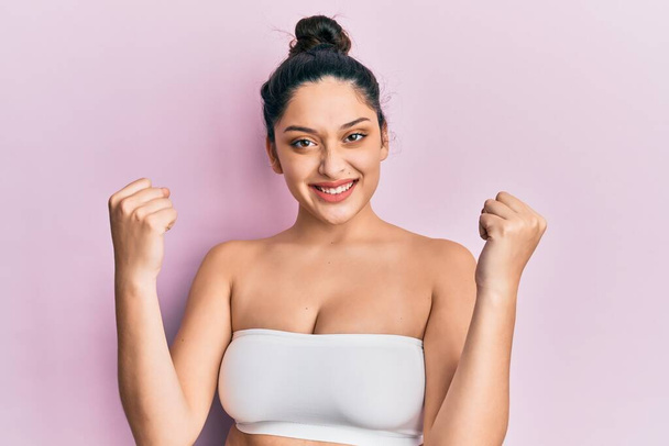 Beautiful middle eastern woman standing wearing a top showing skin screaming proud, celebrating victory and success very excited with raised arms  - Photo, Image