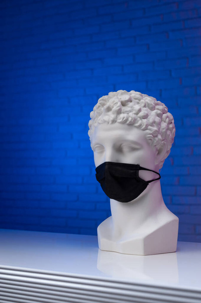 Άγαλμα λευκού γύψου με προστατευτική ιατρική μάσκα μιας χρήσης που καλύπτει το πρόσωπό του - Φωτογραφία, εικόνα