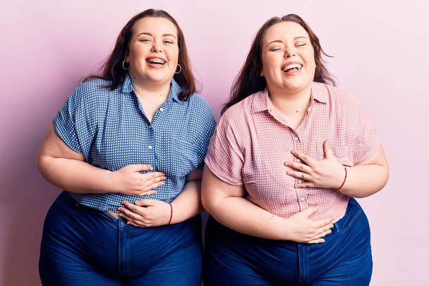 Junge Plus-Size-Zwillinge in lässiger Kleidung lächeln und lachen laut, weil lustig verrückter Witz mit den Händen am Körper.  - Foto, Bild
