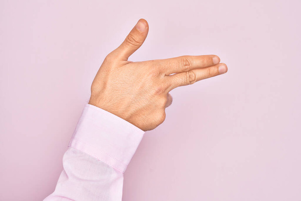 Main de jeune homme caucasien montrant les doigts sur fond rose isolé gesticulant arme à feu avec les doigts, visant symbole de tir - Photo, image