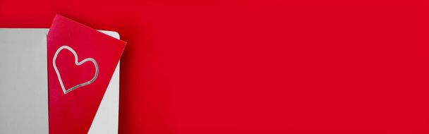 banner de formato largo tarjeta de papel alargada roja con corazón de plata en sobre blanco sobre fondo rojo. Saludos navideños, contenido visual para el 14 de febrero - Foto, Imagen