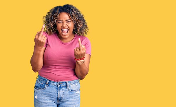 Young african american plus size woman wearing casual clothes showing middle finger doing fuck you bad expression, provocation and rude attitude. screaming excited  - 写真・画像