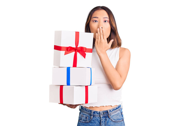 Giovane bella ragazza cinese in possesso di regalo che copre la bocca con la mano, scioccato e spaventato per errore. espressione sorpresa  - Foto, immagini
