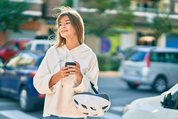 Caucasian sporty teenager girl holding bike helmet using smartphone at the city. - 写真・画像