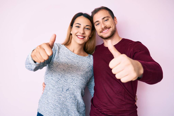 Beautiful couple wearing casual clothes approving doing positive gesture with hand, thumbs up smiling and happy for success. winner gesture.  - Photo, Image