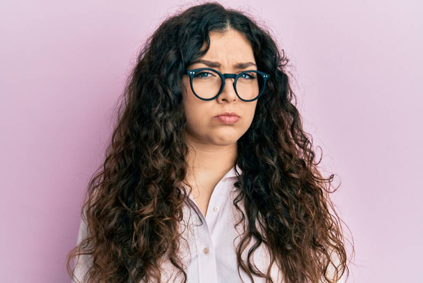 Young brunette woman with curly hair wearing casual clothes and glasses skeptic and nervous, frowning upset because of problem. negative person.  - Photo, Image