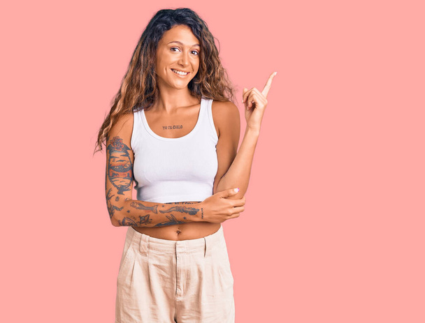 Young hispanic woman with tattoo wearing casual clothes smiling happy pointing with hand and finger to the side  - Foto, imagen