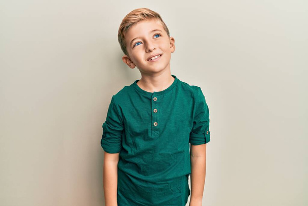 Kleine blanke jongen draagt casual kleding op zoek naar kant, ontspannen profiel poseren met een natuurlijk gezicht en zelfverzekerde glimlach.  - Foto, afbeelding
