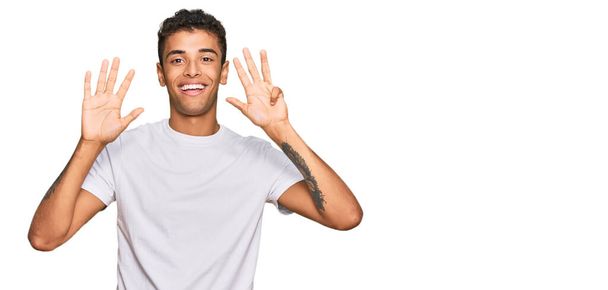 Joven hombre afroamericano guapo usando camiseta blanca casual mostrando y apuntando hacia arriba con los dedos número nueve mientras sonríe confiado y feliz.  - Foto, Imagen