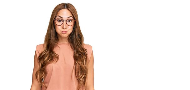 Young hispanic woman wearing casual clothes and glasses puffing cheeks with funny face. mouth inflated with air, crazy expression.  - Photo, Image