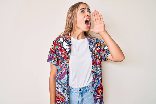 Young beautiful blonde woman wearing modern clothes shouting and screaming loud to side with hand on mouth. communication concept.  - Photo, Image