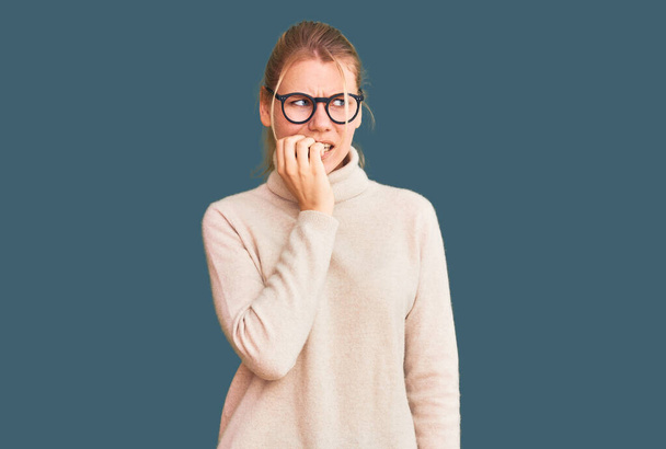 Young beautiful blonde woman wearing turtleneck sweater and glasses looking stressed and nervous with hands on mouth biting nails. anxiety problem.  - Photo, Image