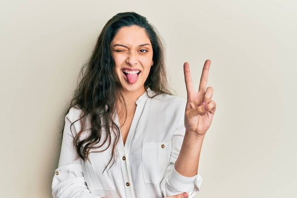 Beautiful middle eastern woman wearing casual clothes smiling with happy face winking at the camera doing victory sign. number two.  - Photo, Image
