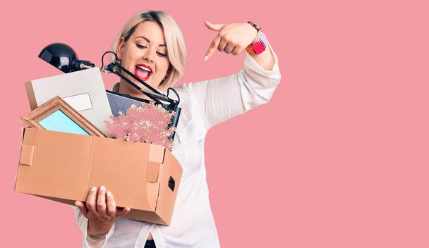 Young blonde plus size woman fired holding box smiling happy pointing with hand and finger  - Photo, image
