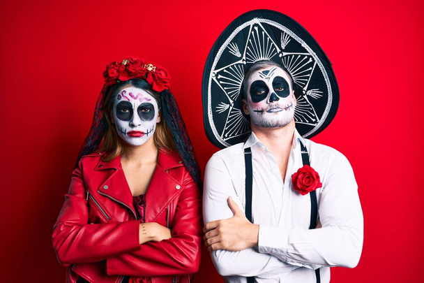Couple wearing day of the dead costume over red skeptic and nervous, disapproving expression on face with crossed arms. negative person.  - Photo, image