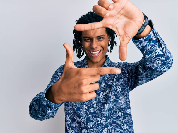 Joven hombre afroamericano con camisa estilo 80 sonriendo haciendo marco con manos y dedos con la cara feliz. concepto de creatividad y fotografía.  - Foto, Imagen