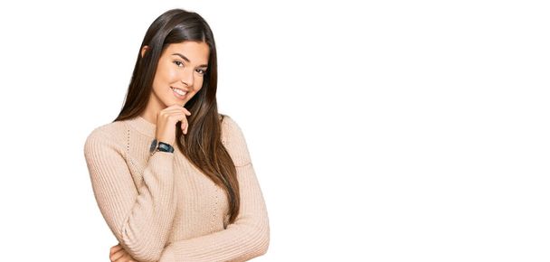 Young brunette woman wearing casual winter sweater looking confident at the camera smiling with crossed arms and hand raised on chin. thinking positive.  - Photo, Image