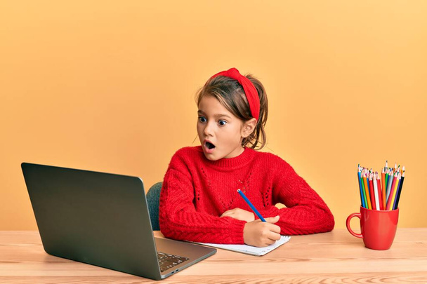 Kis gyönyörű lány tanul számítógépes laptop fél, és sokkolt a meglepetés és csodálkozó kifejezés, félelem és izgatott arc.  - Fotó, kép