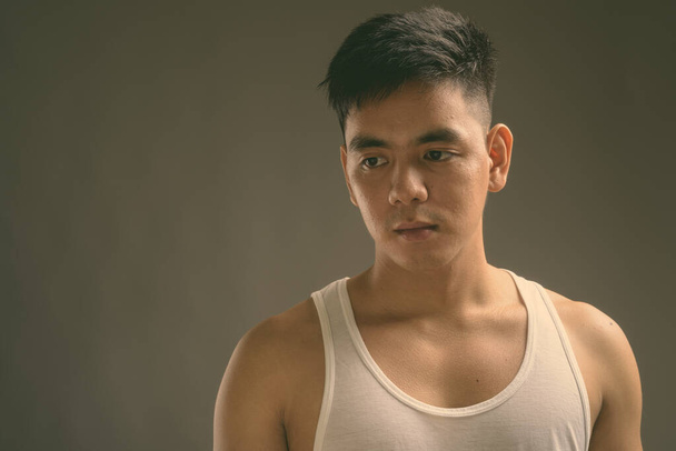 Joven guapo asiático hombre usando camiseta sin mangas contra fondo gris - Foto, Imagen