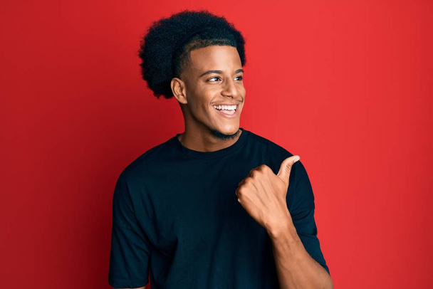 Hombre afroamericano con el pelo afro usando ropa casual apuntando el pulgar hacia el lado sonriendo feliz con la boca abierta  - Foto, imagen