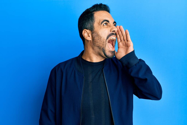 Junger hispanischer Mann in lässiger Kleidung, der schreit und laut mit der Hand auf den Mund schreit. Kommunikationskonzept.  - Foto, Bild