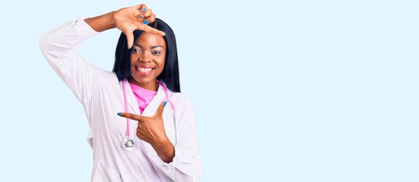 Genç Afro-Amerikan kadın doktor steteskobu takmış gülümsüyor ve elleri ve parmakları mutlu yüzlü bir çerçeve yapıyor. yaratıcılık ve fotoğrafçılık kavramı.  - Fotoğraf, Görsel