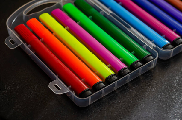 Farbige Filzstifte im Kunststoffbehälter auf schwarzem Tisch. Kreativität Zeichnung Konzept. Selektiver Fokus. - Foto, Bild