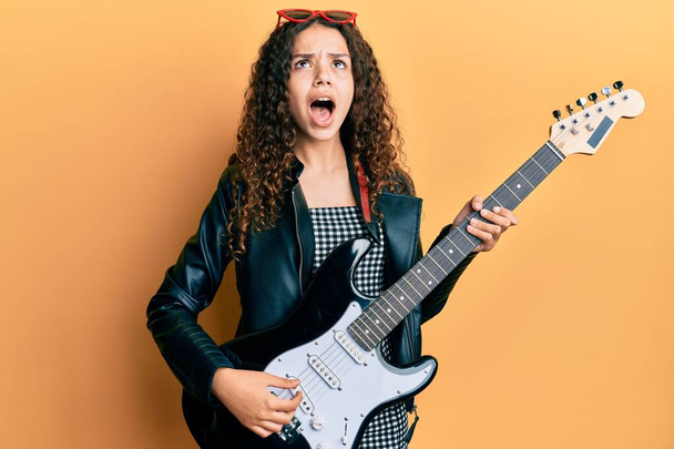 Genç İspanyol kız elektro gitar çalıyor kızgın ve deli gibi bağırıyor sinirli ve öfkeli, öfkeyle bağırıyor..  - Fotoğraf, Görsel