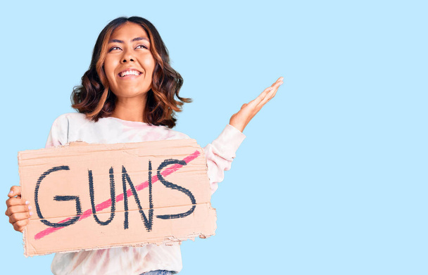 Young beautiful mixed race woman holding no guns warning banner celebrating victory with happy smile and winner expression with raised hands  - Photo, Image