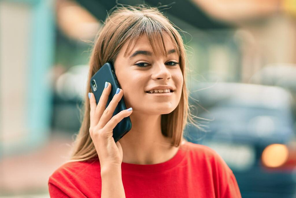 Καυκάσια έφηβη χαμογελά ευτυχισμένη μιλώντας στο smartphone στην πόλη. - Φωτογραφία, εικόνα