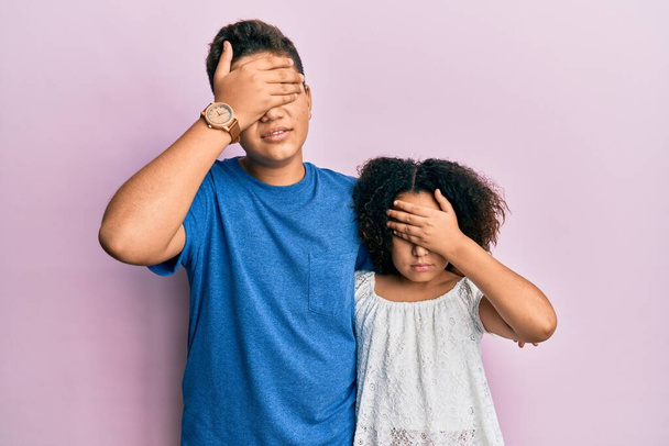Молодая латиноамериканская семья брата и сестры в повседневной одежде вместе закрывают глаза рукой, выглядят серьезными и грустными. беспросветная, скрывающая и отвергающая концепция  - Фото, изображение