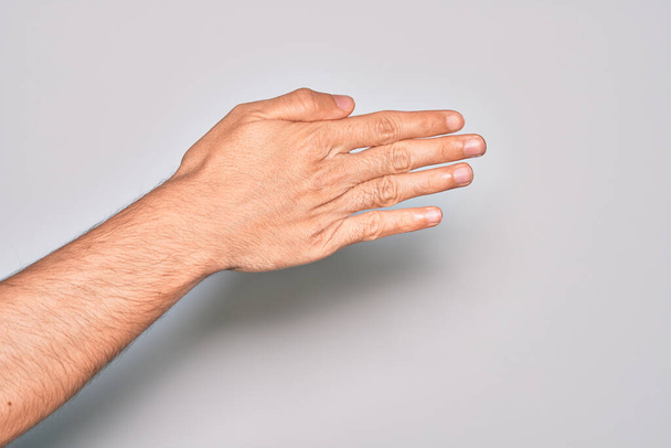 Hand eines kaukasischen jungen Mannes mit Fingern über isoliertem weißem Hintergrund, der sich streckt und mit geöffneter Hand nach Handschlag greift, Zeigen des Handrückens - Foto, Bild