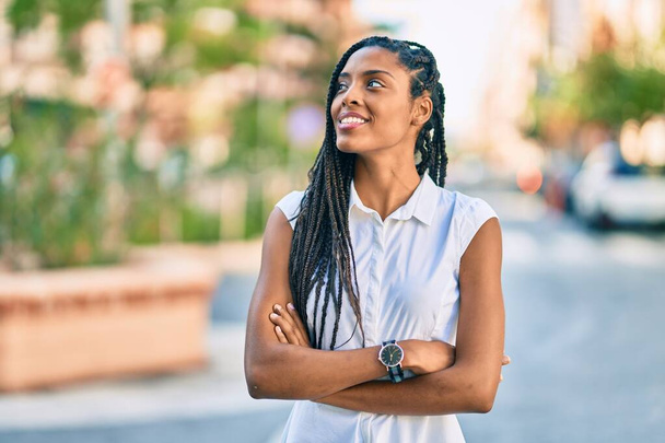 Joven mujer afroamericana con los brazos cruzados sonriendo feliz en la ciudad. - Foto, Imagen