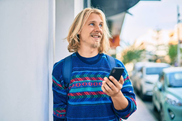 Молодий скандинавський студент усміхається щасливий, використовуючи смартфон у місті
. - Фото, зображення