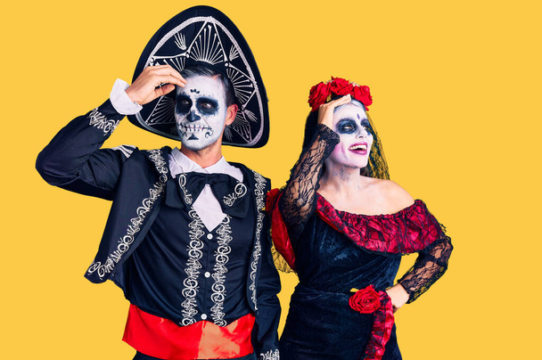 Jong paar dragen mexicaanse dag van het dode kostuum over de achtergrond glimlachen zelfverzekerd aanraken haar met de hand omhoog gebaar, poseren aantrekkelijk en modieus  - Foto, afbeelding