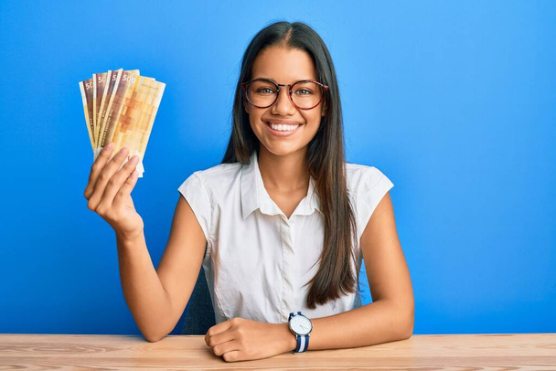Mooie Latijns-Amerikaanse vrouw met 500 Noorse kroon bankbiljetten die er positief en gelukkig uitzien en glimlachend met een zelfverzekerde glimlach die tanden laat zien  - Foto, afbeelding