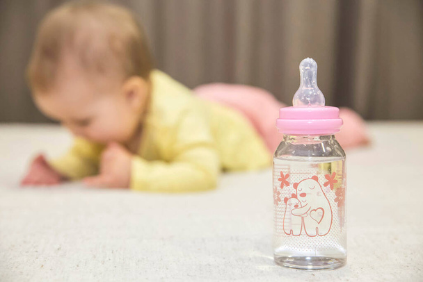 bebé se acuesta en la cama junto a una botella de agua - Foto, Imagen