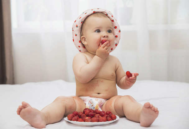lindo bebé manchado en un sombrero con fresas pintadas comiendo bayas - Foto, Imagen