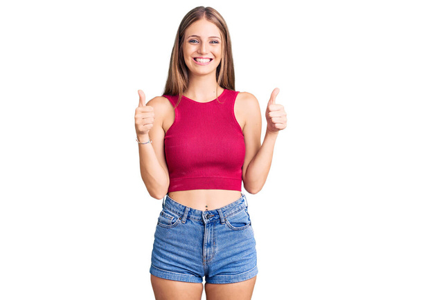 Young beautiful blonde woman wearing elegant summer shirt success sign doing positive gesture with hand, thumbs up smiling and happy. cheerful expression and winner gesture.  - Photo, image