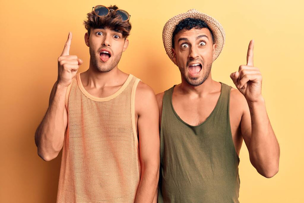 Молода пара геїв носить літній одяг, вказуючи пальцем на успішну ідею. вичерпаний і щасливий. номер один
.  - Фото, зображення