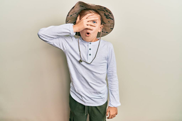 Pequeno garoto caucasiano vestindo chapéu de explorador espreitando em choque cobrindo rosto e olhos com a mão, olhando através dos dedos com medo  - Foto, Imagem
