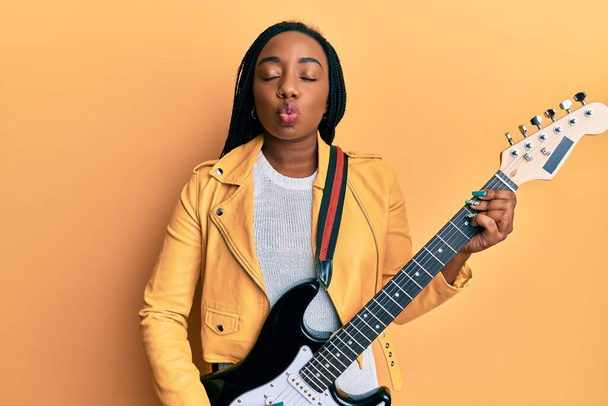 Young african american woman playing electric guitar looking at the camera blowing a kiss being lovely and sexy. love expression.  - Photo, Image