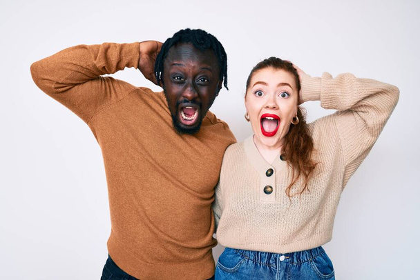Interracial couple wearing casual clothes crazy and scared with hands on head, afraid and surprised of shock with open mouth  - Photo, Image