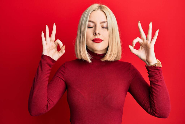 Young blonde woman wearing casual clothes relaxed and smiling with eyes closed doing meditation gesture with fingers. yoga concept.  - Фото, зображення