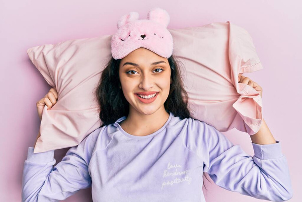 Красивая женщина с Ближнего Востока в маске для сна и пижаме спит на подушке, улыбаясь со счастливой и прохладной улыбкой на лице. показывая зубы.  - Фото, изображение