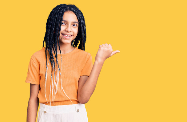 Aranyos afro-amerikai lány alkalmi ruhát visel mosolygós boldog arc néz, és rámutatva oldalra hüvelykujjal felfelé.  - Fotó, kép