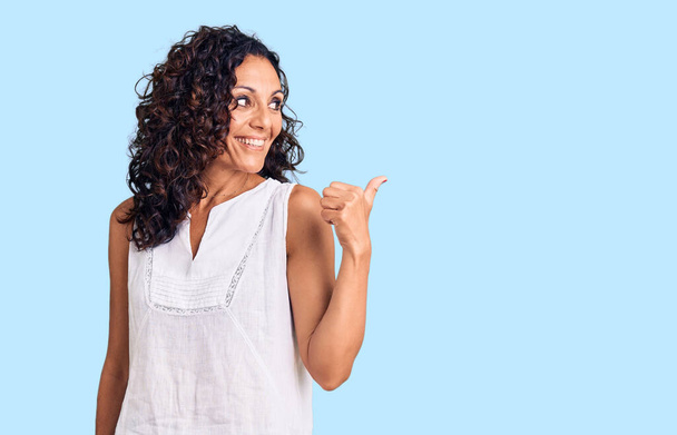 Middle age beautiful woman wearing casual sleeveless t shirt smiling with happy face looking and pointing to the side with thumb up.  - Photo, Image