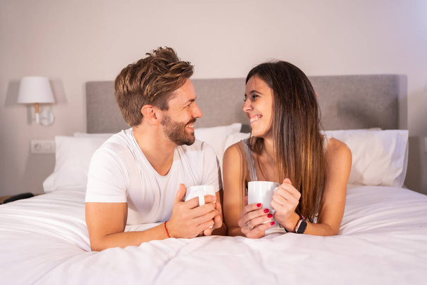 Pijamalı bir çiftin otel yatağında kahvaltı edişine benziyor. Aşık bir çiftin yaşam tarzı. - Fotoğraf, Görsel